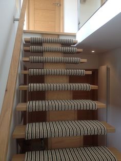 a stair case with black and white striped carpet on the bottom, next to a wooden handrail