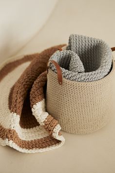 two crocheted baskets sitting next to each other on a white counter top with a brown leather handle