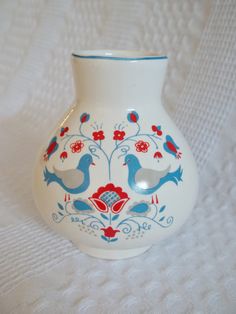 a white vase with blue and red designs on the side sitting on a white surface