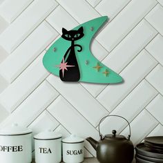 a black cat sitting on top of a green shelf next to two teapots