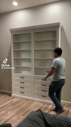 a man standing in front of a large white bookcase with drawers on it's sides