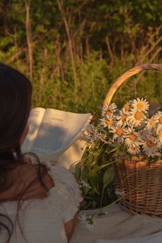 a woman reading a book with daisies in a basket