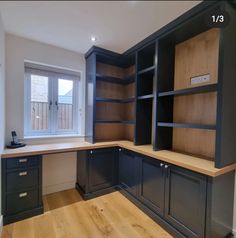 an empty kitchen with black cabinets and wood flooring on the walls, in front of a window