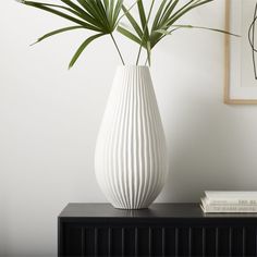 a white vase sitting on top of a black table next to a book and plant