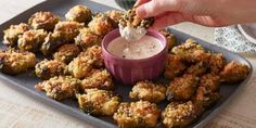 a person dipping something in a small bowl on top of some fried food with ranch dressing