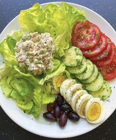 a white plate topped with lettuce, tomatoes and cucumber next to olives