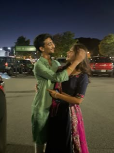 two people standing in the middle of a parking lot at night, one holding the other's hand