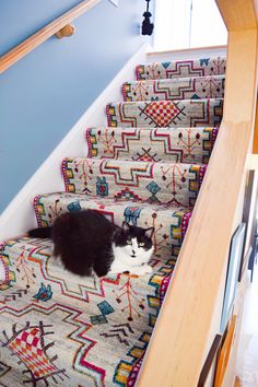 a black and white cat is sitting on the carpeted stair treads in a home