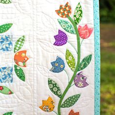 a quilted wall hanging with flowers and leaves on the outside, in front of a grassy area