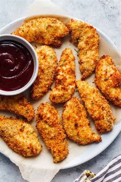 fried chicken sticks with ketchup on a white plate next to a striped napkin