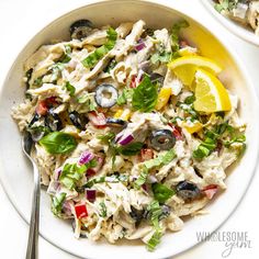 a white bowl filled with pasta salad next to a fork and lemon wedge on the side