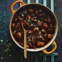 a pot filled with meatballs and sauce on top of a wooden table next to an orange spoon