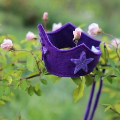 a purple hat with a star on it is hanging from a branch in front of some pink flowers