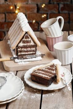 a slice of cake on a plate next to a gingerbread house and cup of coffee