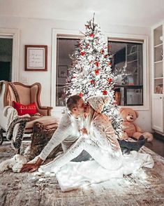 a man and woman kissing in front of a white christmas tree with red berries on it