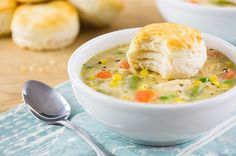 a white bowl filled with soup next to a spoon and some bread on top of it