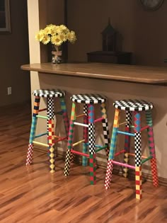 three colorful stools sitting on top of a hard wood floor next to a counter