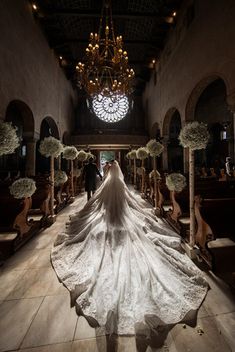 the bride is walking down the aisle with her long veil flowing in front of her