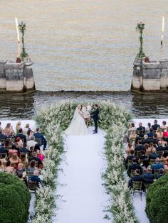 a couple getting married in front of an outdoor ceremony with flowers and greenery on the aisle