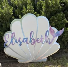 a large white shell with the word elizabeth painted on it in front of some bushes