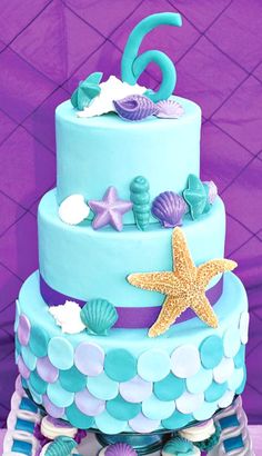 a three tiered blue cake with sea shells and starfish on the top layer