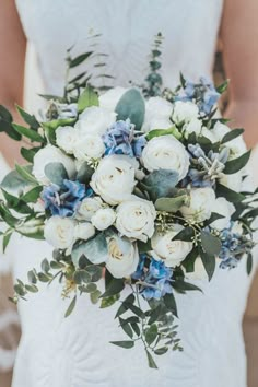 a bridal holding a bouquet of white and blue flowers in her hands with greenery