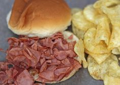 there is a sandwich and potato chips on the table next to each other with meat