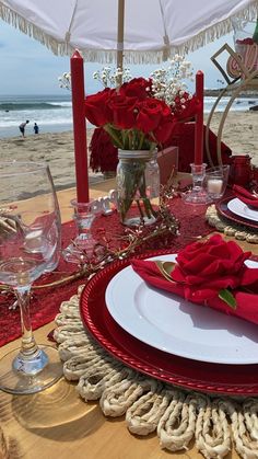 the table is set with red roses and place settings for two people at the beach