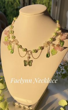 a necklace with green and pink beads on a white mannequin head stand in front of greenery