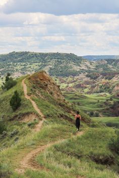 a person walking down a dirt path on top of a grass covered hill with hills in the background