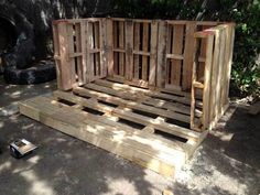 a bed made out of wooden pallets sitting on the ground next to a tree