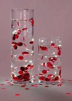 two tall vases filled with water and red berries on the inside, surrounded by confetti