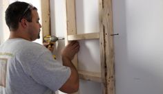 a man is working on an unfinished wall with screwdrivers and wood planks