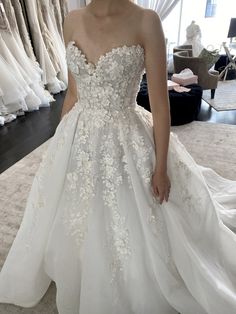 a woman standing in front of a rack of wedding gowns