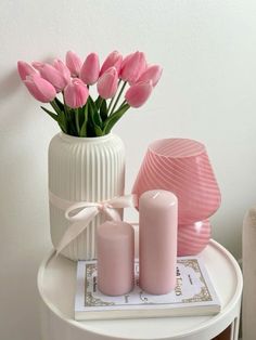 pink tulips are in a white vase on a small table next to candles