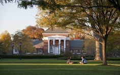 two people sitting on the grass in front of a large building with columns and pillars