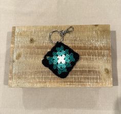 a square keychain with a crocheted flower in the center on a wooden board