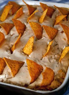 a baking dish filled with nachos covered in white sauce and tortilla chips