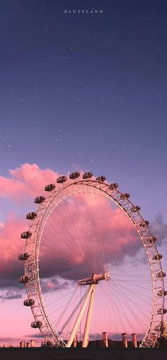 a large ferris wheel sitting in the middle of a field under a pink sky with clouds