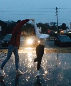 two people jumping in the air on a wet street at night with cars behind them