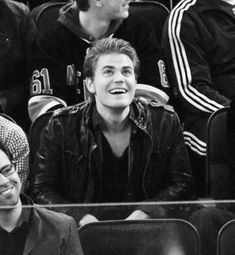 two men sitting next to each other at a basketball game, one smiling and the other laughing