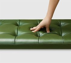 a person touching the foot of a green leather bench