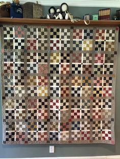 an old quilt hanging on a wall in a room with bookshelves and other items