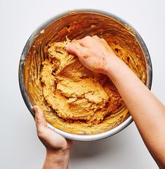 two hands reaching into a mixing bowl filled with yellow cake batter on a white surface