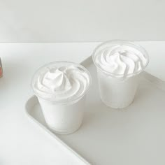 two plastic cups filled with whipped cream on top of a white tray