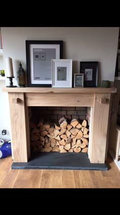 a fire place with logs stacked in front of it and framed pictures on the wall