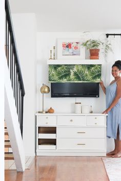 a woman standing in front of a flat screen tv mounted on a wall next to a stair case