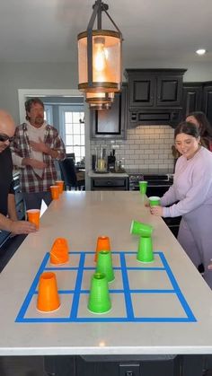 a group of people standing around a kitchen table with cups on it and an orange cup in the middle