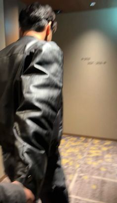 a man in a black leather jacket is walking down the hall with his luggage and looking off into the distance