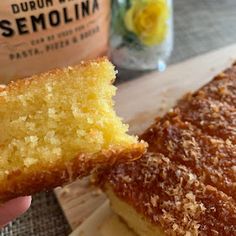 a person holding a piece of cake in front of a jar of lemonade on a cutting board